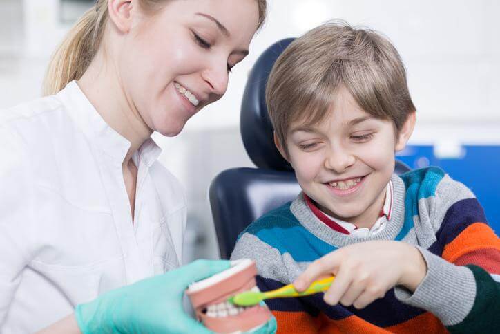 A dental assistant shows a child how to brush his teeth