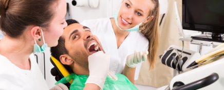 Dentist with assistant examining the oral cavity of male patient at dental clinic