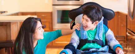 Nine year old disabled boy in wheelchair laughing with teen sister in kitchen