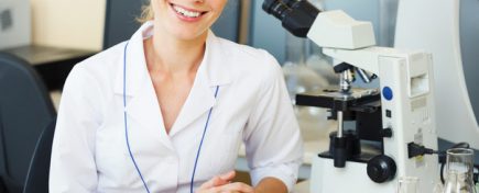 Portrait of beautiful young woman in a laboratory sitting on her workplace looking at camera