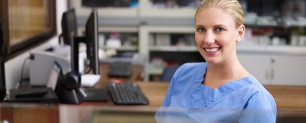 Young woman at work as receptionist and nurse in hospital, looking at camera