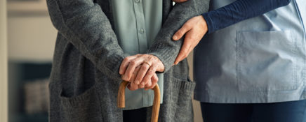 Senior man and young personal support worker holding hands on walking stick, closeup