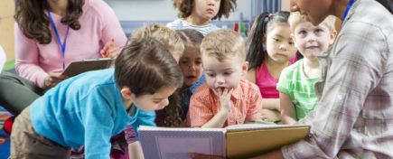 Early Childcare Assistant reads children a book during story time stock photo
