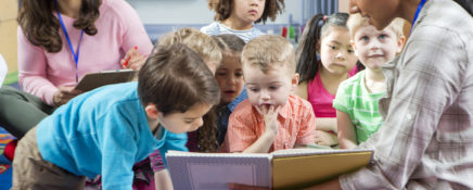 Early Childcare Assistant reads children a book during story time stock photo