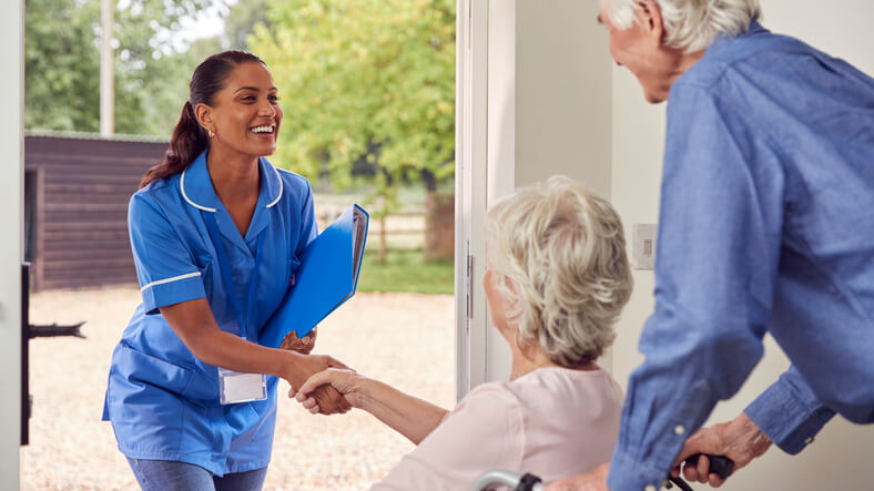 Female PSW greeting a senior woman in a wheelchair while her male companion holds the wheelchair handles