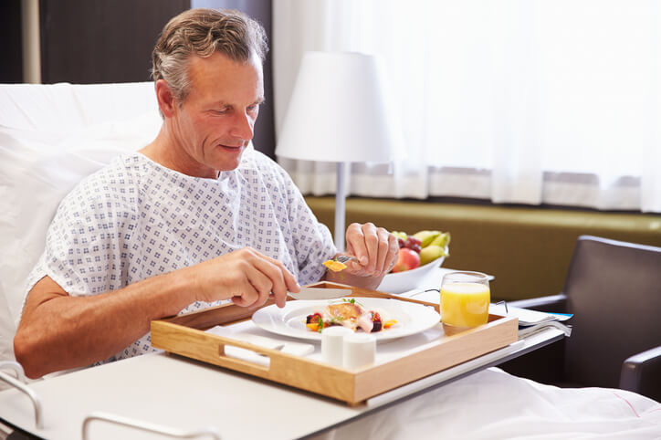 A hospital patient enjoys a meal in bed, served by a Food Services Worker, highlighting the healthcare aspect of a Food Services Worker's career.