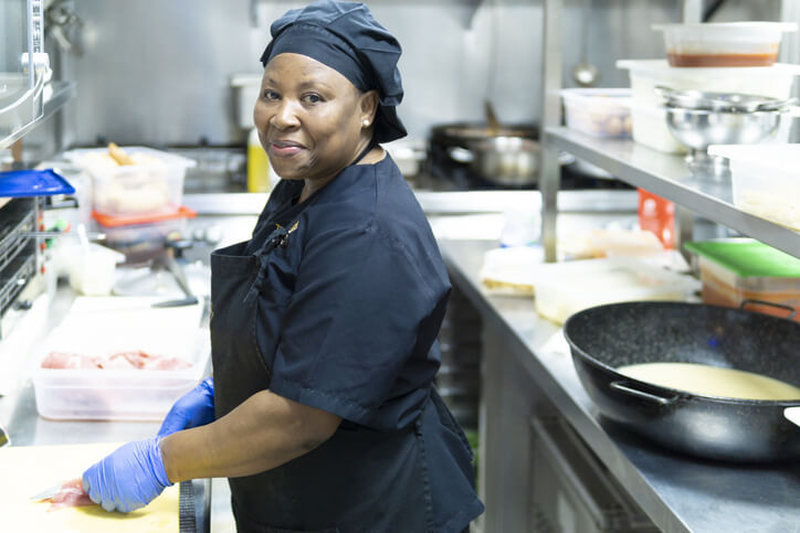 A chef in a commercial kitchen prepares a dish with care, representing the culinary skills required in a Food Services Worker’s career.