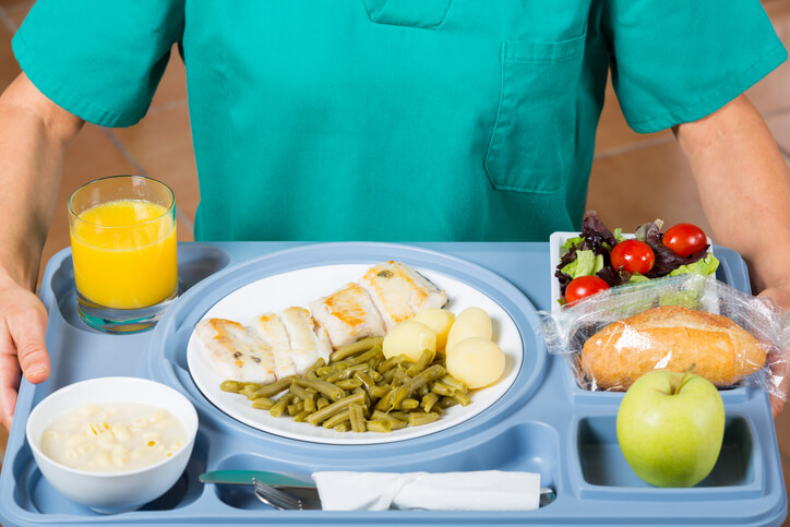 A Food Services Worker in scrubs presents a balanced meal tray, emphasizing the nutritional care element of a Food Services Worker's career.