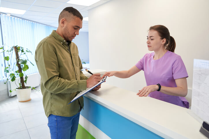 A female dental administrator assisting a patient with paperwork after completing her dental administration course