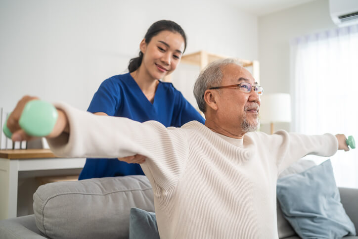 A physiotherapy assistant program grad helping an elderly patient to lift weights