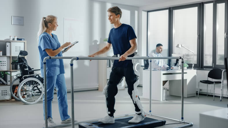 A physiotherapy assistant program grad helping a patient walk in a high-tech clinic