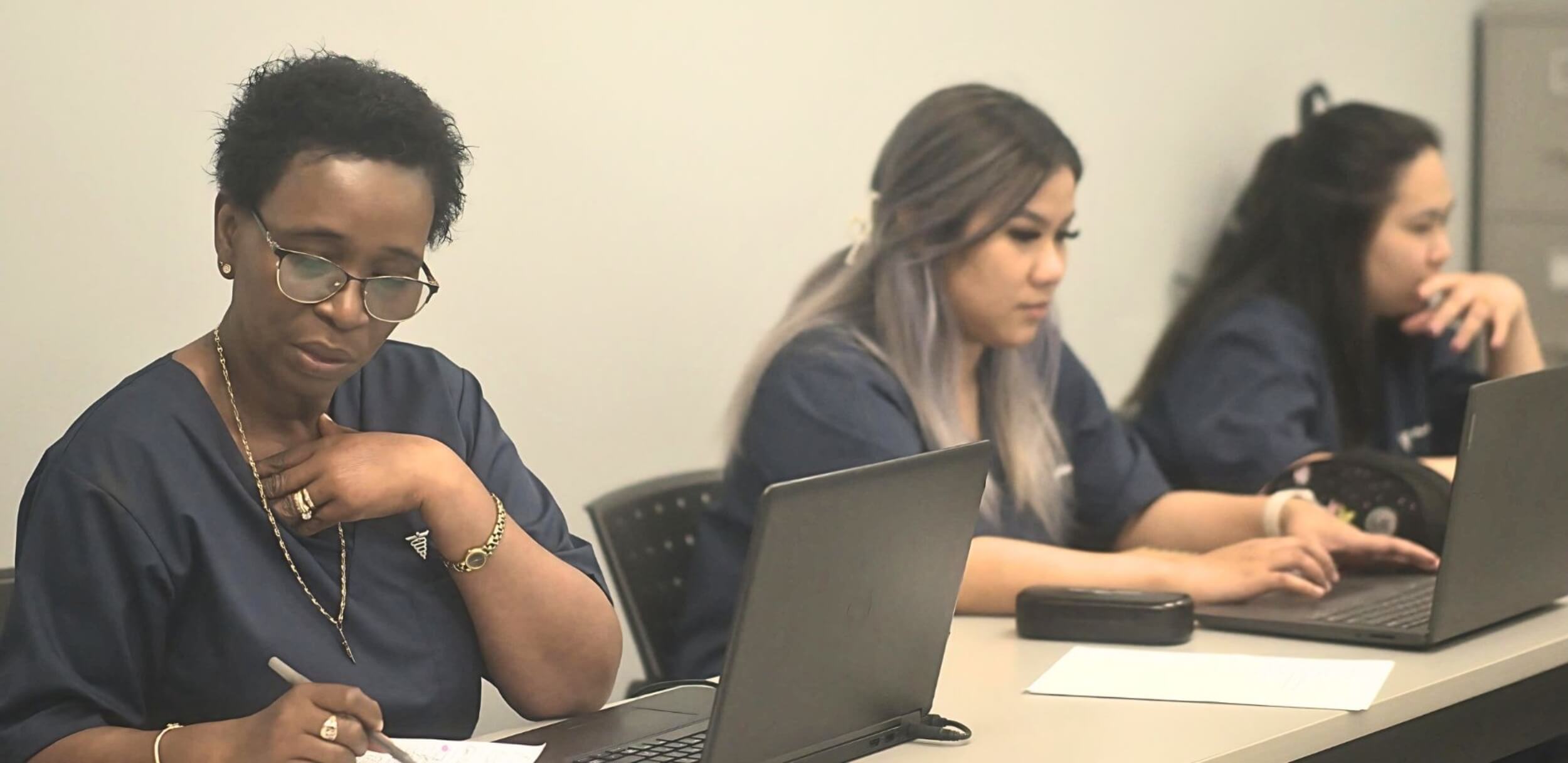 Three female students taking notes during a class while taking their dental administration course