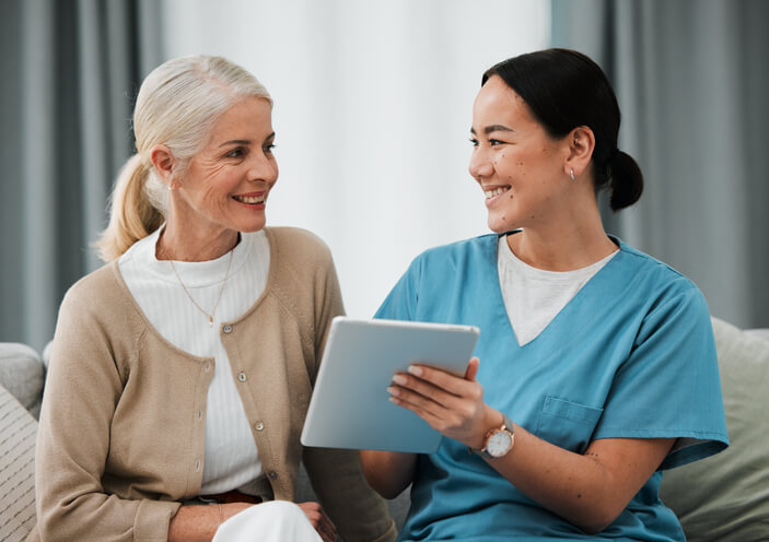 A smiling female personal support worker interacting with an elderly female client on a couch