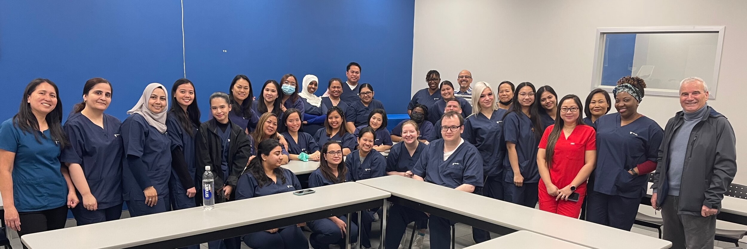 A group of students and instructors from a Career College pose in a classroom, all smiling at the camera.