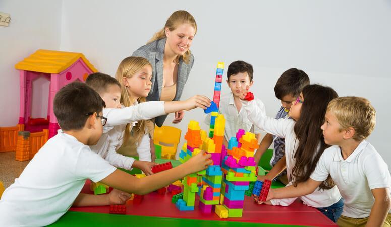 A daycare setting featuring an early childcare assistant guiding children through a collaborative learning activity.