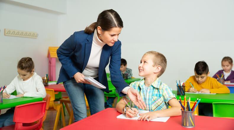 A smiling female early childcare assistant helping a male learner during a lesson.