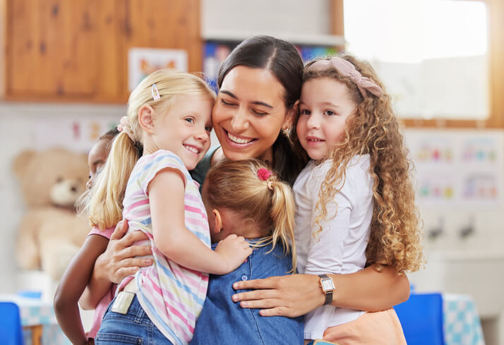 An early childhood assistant hugging students
