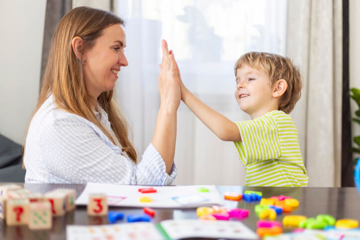 An early childhood assistant giving a student a high five at a table