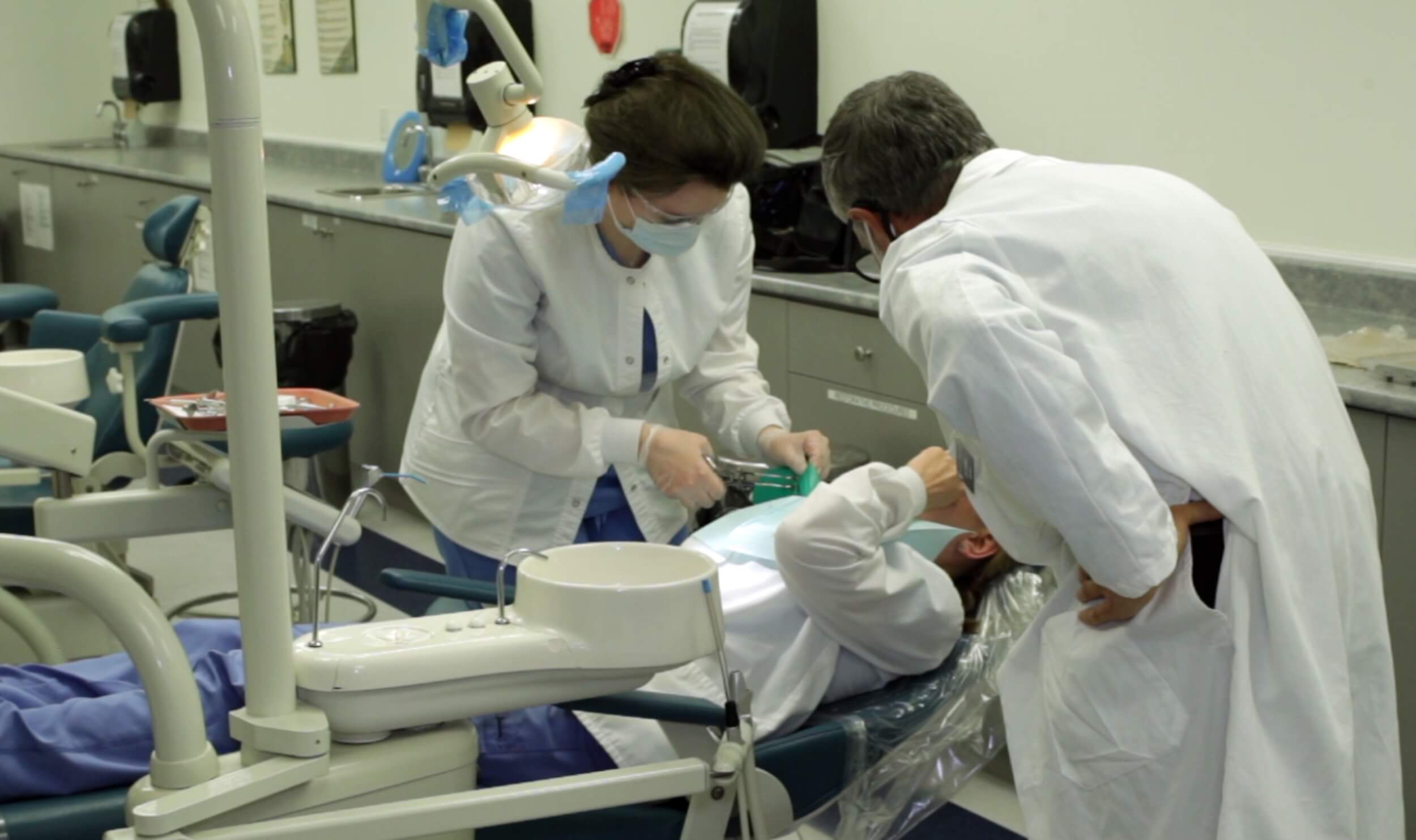 Dental assistant job duties shown as a dental assistant and dentist work together during a procedure on a patient, with the assistant preparing tools and materials.